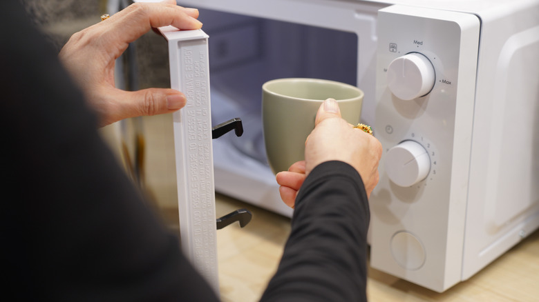 A person placing a mug in an open microwave