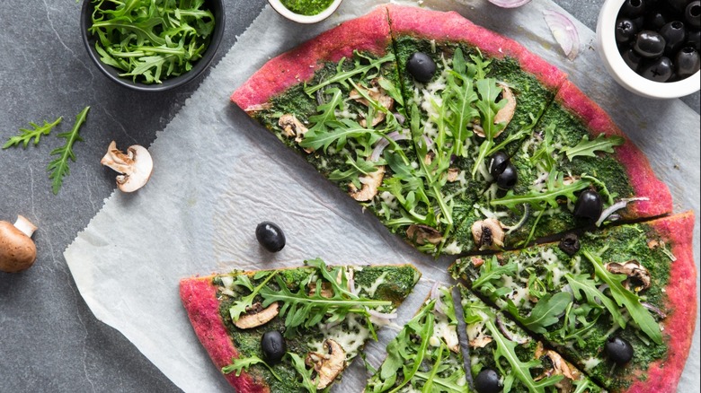 A beet crust pizza with green toppings sitting on a table.