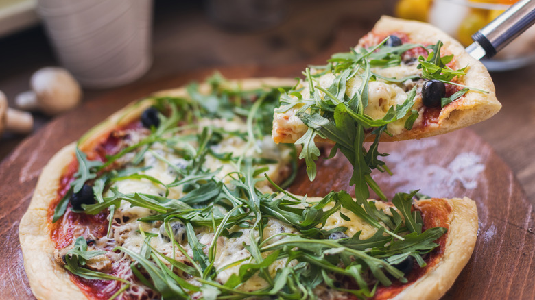 A slice of arugula-topped pizza being lifted up