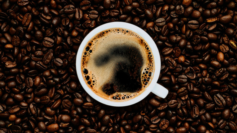 A cup of coffee resting on a pile of roasted coffee beans.