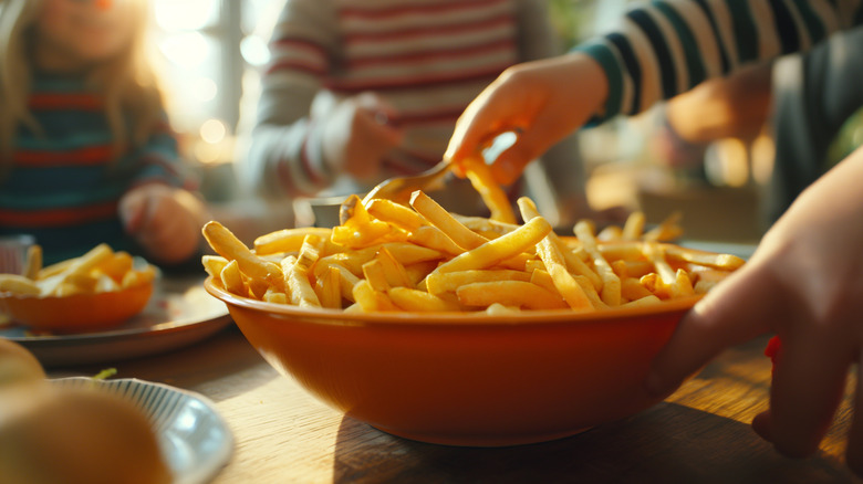 A person serving up french fries in a brown bowl