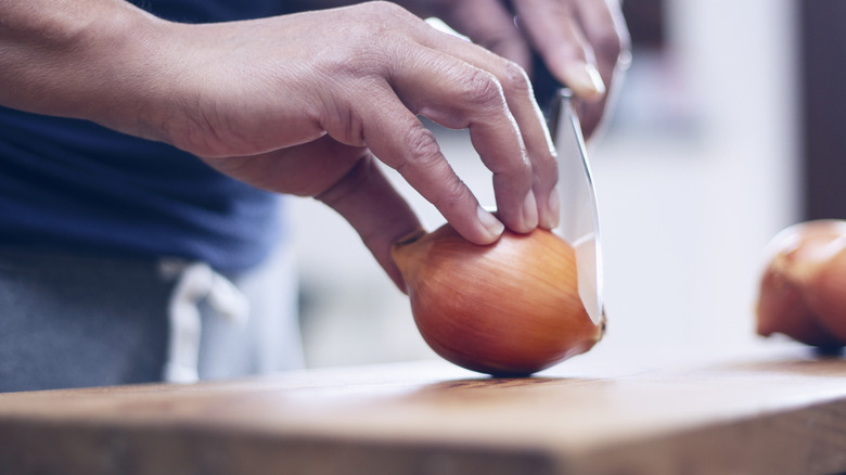 Hands slicing yellow onion with kitchen knife