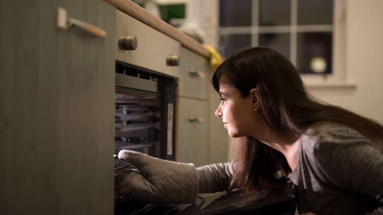 Woman with an oven mit reaching into the oven for a pan