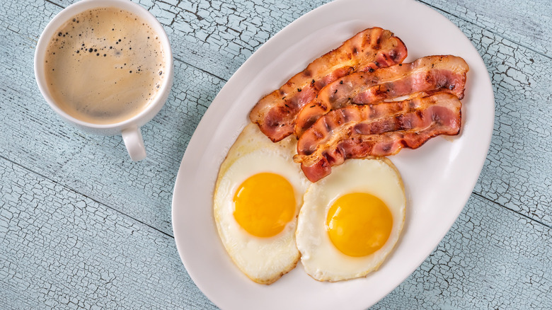 Plate of over-easy eggs with a side of bacon and cup of coffee