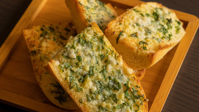 Slices of homemade garlic bread on a wooden serving platter.