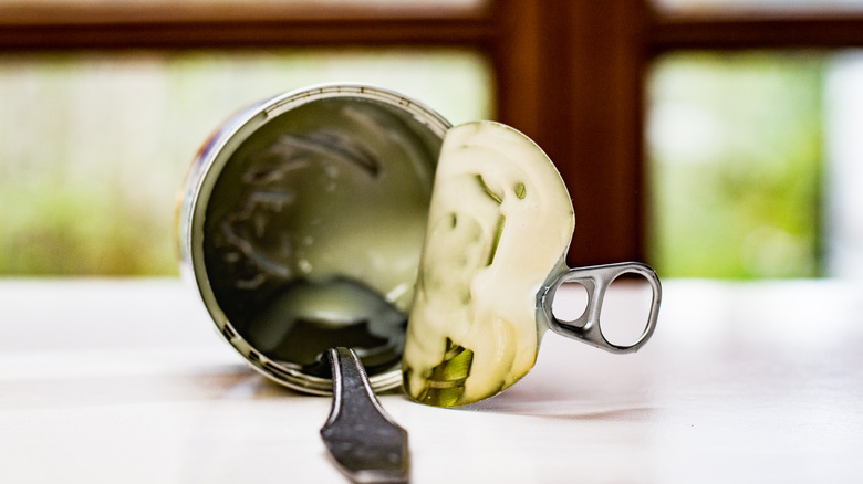 Empty can of evaporated milk on a table with a silver spoon inside of it