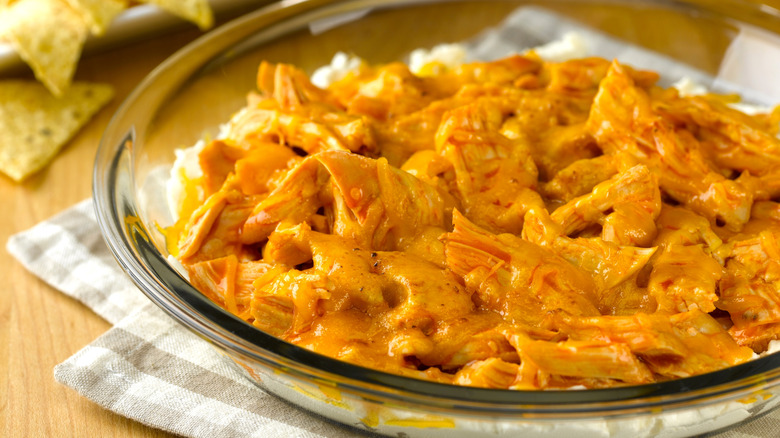 A pie plate of buffalo chicken dip with tortilla chips in the background