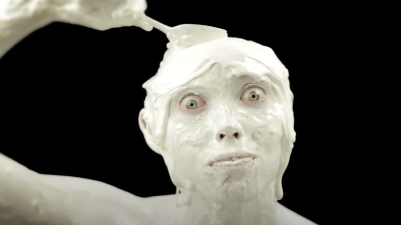 A man covered in ice cream raises a spoon to his head