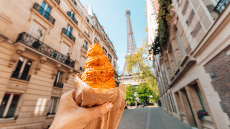 A person holding a croissant in front of the Eiffel Tower.