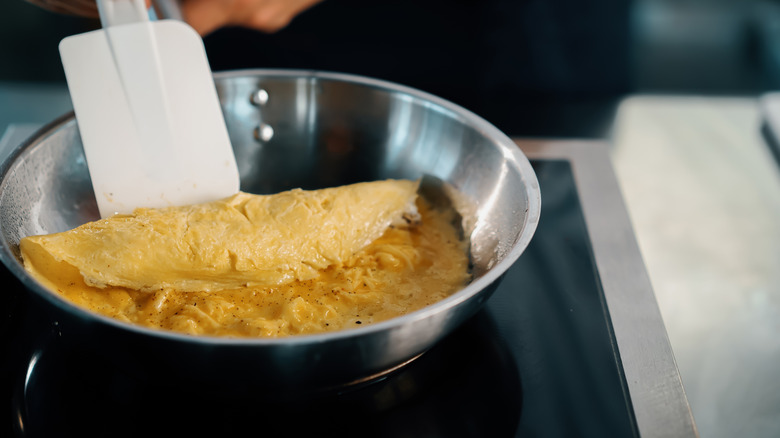 A chef working a French omelette with a spatula in a metal bowl