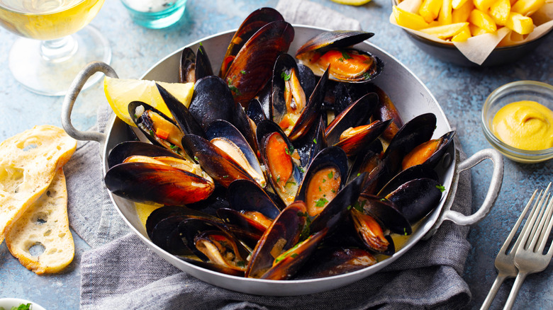 Fresh cooked mussels in a pan with fries and bread