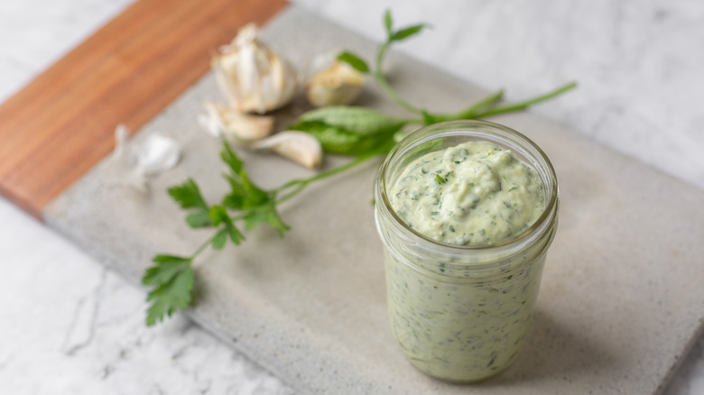 creamy green goddess dressing in a mason jar beside fresh garlic and herbs