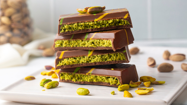 Four pieces of the Dubai pistachio chocolate on a white plate surrounded by pistachios