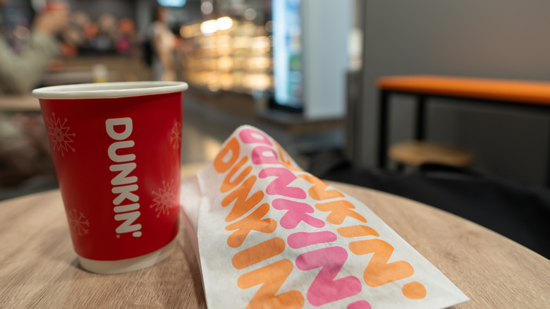 A red Dunkin' Donuts coffee cup and a pastry bag on a wooden table