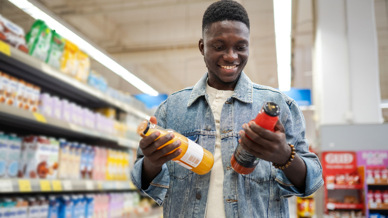 A man looking at two bottled drink options at the supermarket