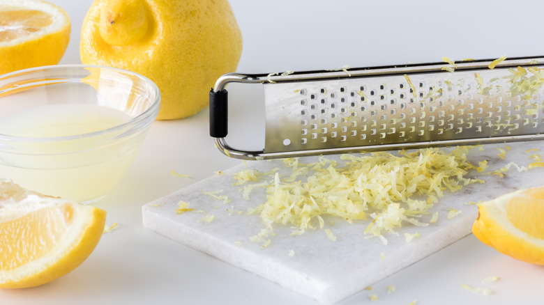 A Microplane with some lemon zest and whole fruit on a board