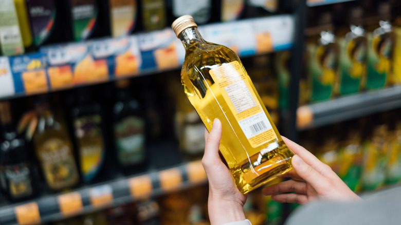 A woman holding a bottle of olive oil in her hand at the grocery store