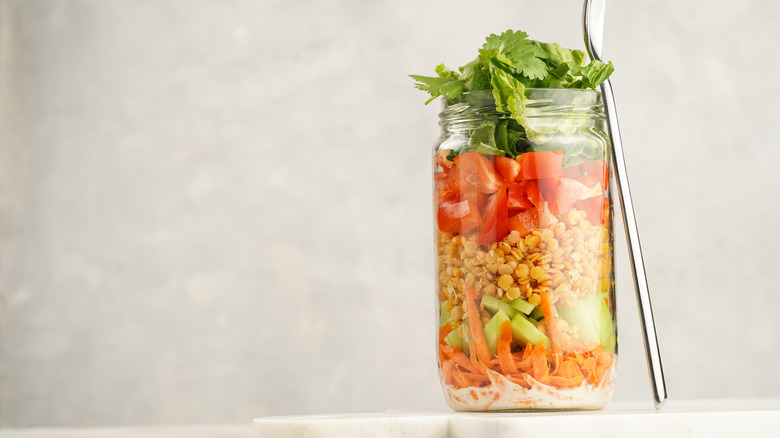 A mason jar of salad with fresh herbs at the top