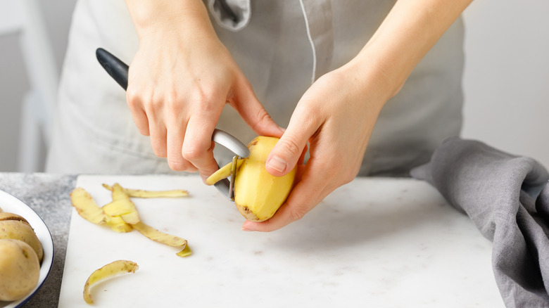 using a vegetable peeler to peel potato