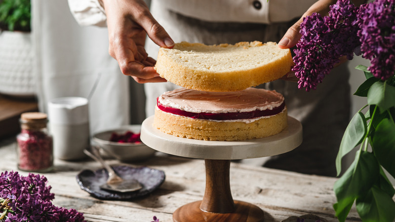 Hands assembling layer cake on cake stand