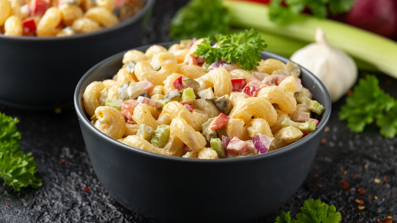 Two black bowls of macaroni salad in with red onion and peppers.