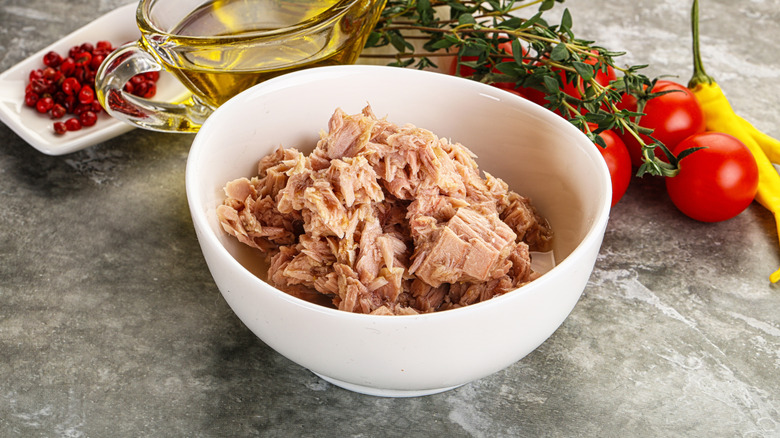 A white bowl of tuna with olive oil and tomatoes.