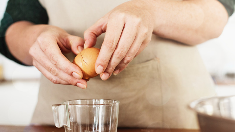 A person peeling open a cracked egg shell over a plastic jug