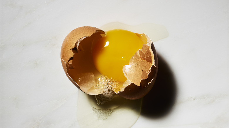 An egg cracked open with yolk visible and whites spilling out