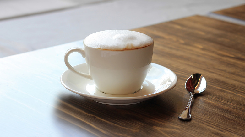 A foamy cappuccino in a small white cup on a table