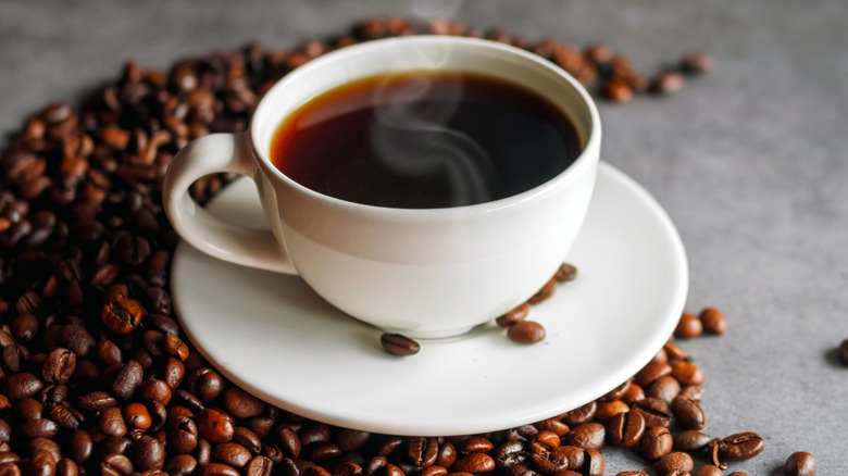 A steaming cup of fresh brewed coffee with coffee beans