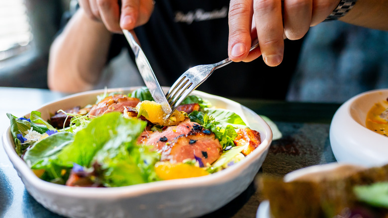 Hands cutting a salad with a knife and fork