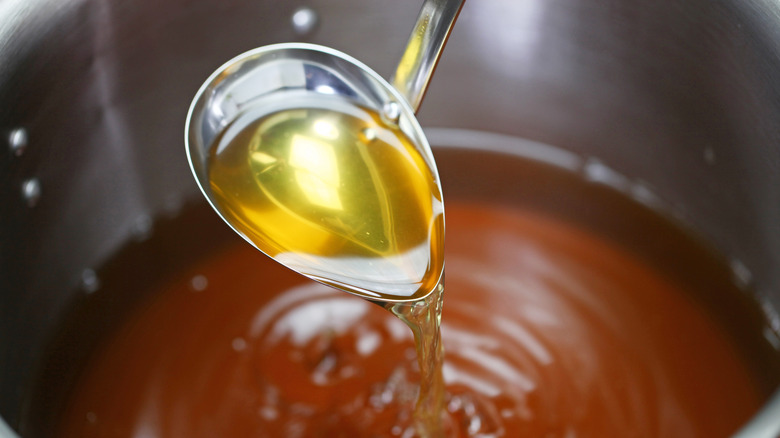 A ladle pouring chicken stock in a pot