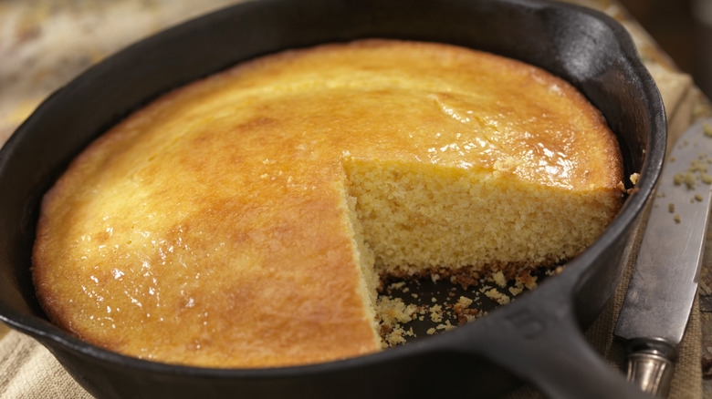 Cornbread in a skillet with one slice cut out of it