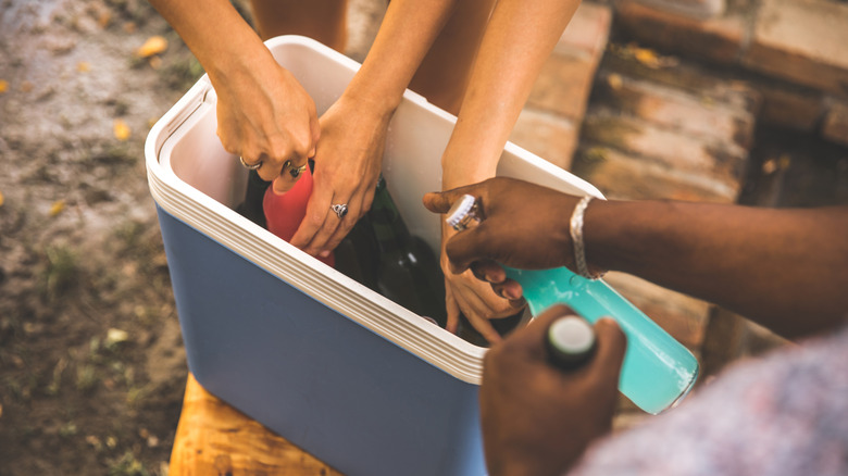 Several people reaching into a drinks cooler and pulling out bottles