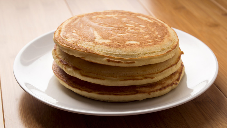 A short stack of fluffy, golden pancakes on a plate on a wooden surface.