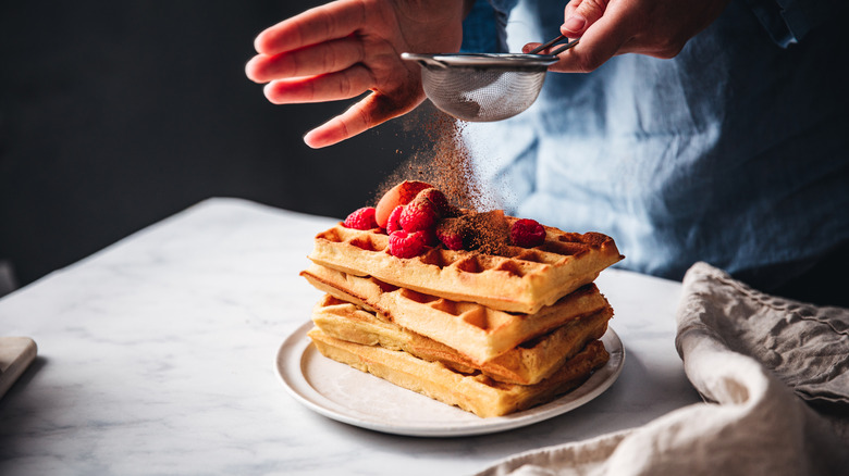 Sprinkling chocolate over waffles topped with fresh berries