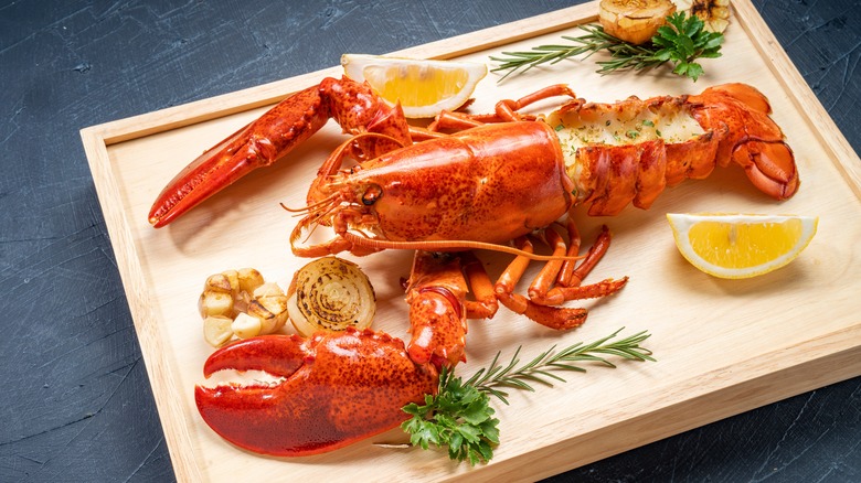 A cooked lobster on a wooden board with lemons and garlic