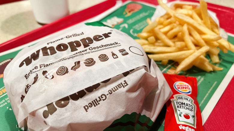 A Whopper cheeseburger in the Burger King paper wrapping, with fries, on a red cafeteria tray