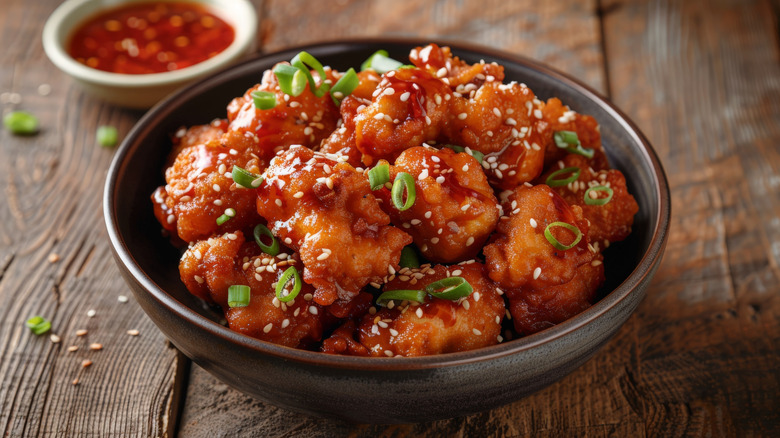 Fried sesame chicken with green onions inside a small bowl.