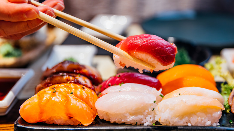 A person eating nigiri sushi rolls with chopsticks