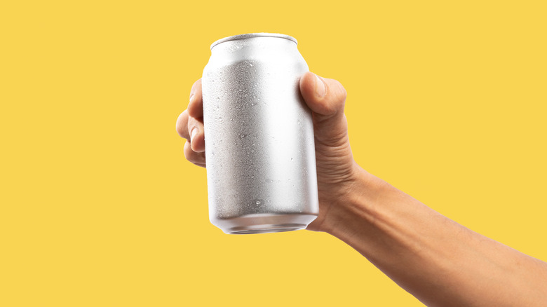 A hand gripping an unnamed soda can against a yellow background.