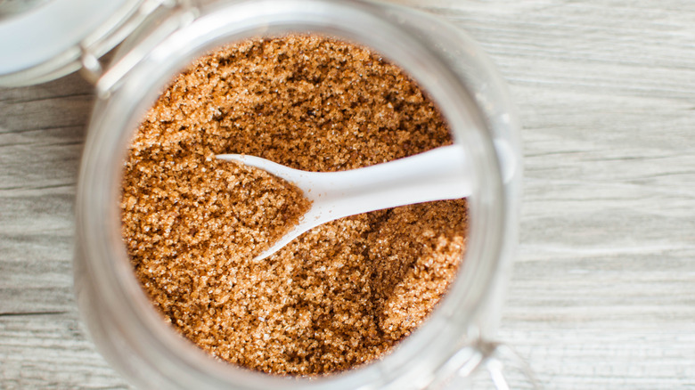 A close up photo of a jar of brown sugar with a spoon in it