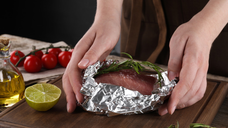 A person wrapping steak in aluminum foil