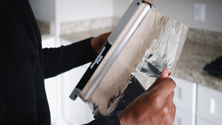 A woman tearing a sheet of aluminum foil