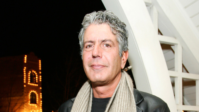 Anthony Bourdain straight-faced wearing a scarf and a black leather jacket