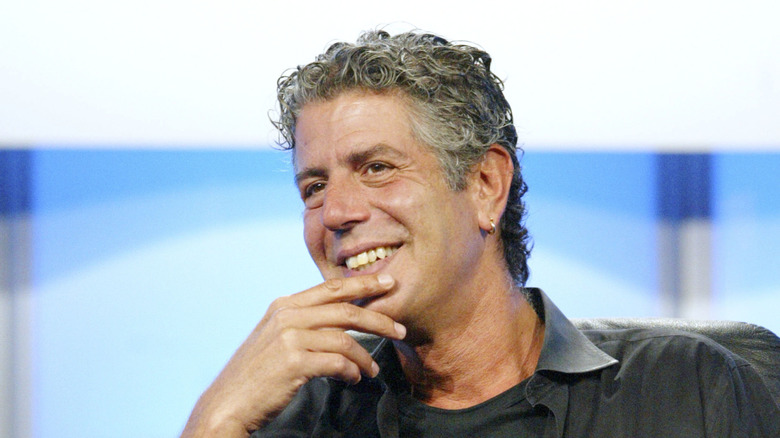 Anthony Bourdain smiling with his hand covering his chin