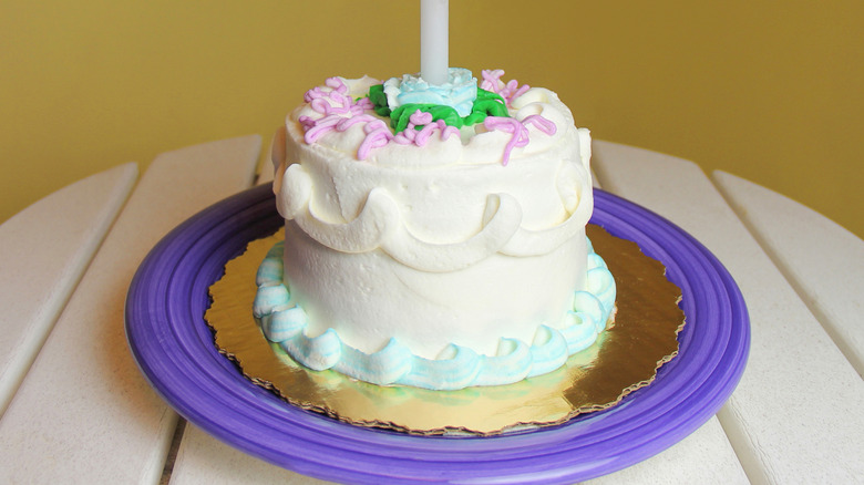 A mini cake with a candle on a purple plate