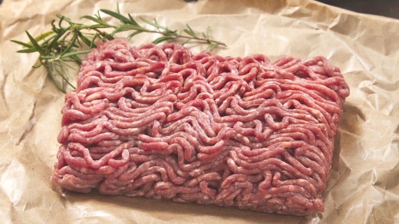 A block of thawed ground beef resting on a sheet of parchment paper.