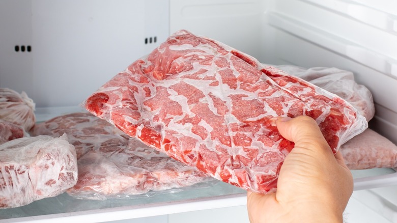 A person pulling wrapped ground beef out of a freezer