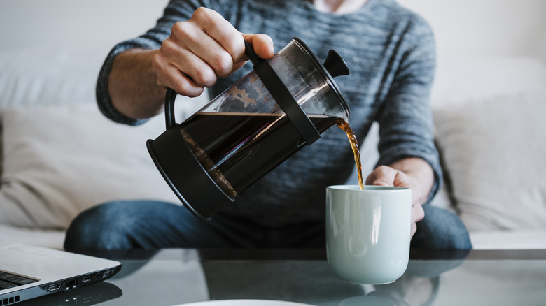 Pouring coffee from a French press into a blue mug